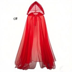 Puede incluir: Una capa roja con capucha que llega hasta el suelo, confeccionada en tela de tul ligera y transparente. La prenda presenta una capucha puntiaguda y un lazo rojo a juego para atar al cuello. El texto C# es visible a la izquierda.