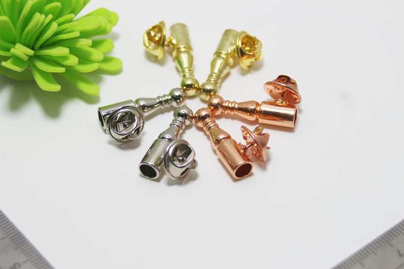 K&ouml;nnte beinhalten: Sortiment von sechs Metall-Stiftverschl&uuml;ssen in verschiedenen Ausf&uuml;hrungen, darunter Gold, Silber und Ros&eacute;gold. Jeder Stiftverschluss hat eine zylindrische Form mit abgerundeter Oberseite und einem Stift an der Unterseite.