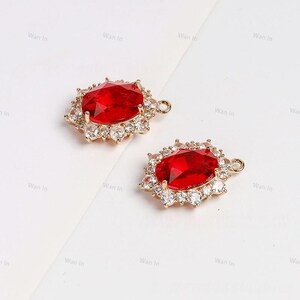 Peut inclure: Deux breloques pendantes dorées avec une grande pierre ovale rouge entourée d'un halo de petits strass transparents. Chaque breloque a une petite boucle en haut pour l'attacher à un collier ou un bracelet.