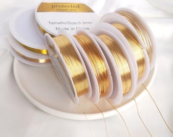 Könnte beinhalten: Mehrere Spulen aus goldfarbenem Kupferdraht mit einer Stärke von jeweils 0,3 mm. Die weißen Kunststoffspulen sind in einer Gruppe angeordnet, wobei das obere Etikett deutlich den Text 'protected copper wire' und 'Tamaño/Size:0.3mm' zeigt.