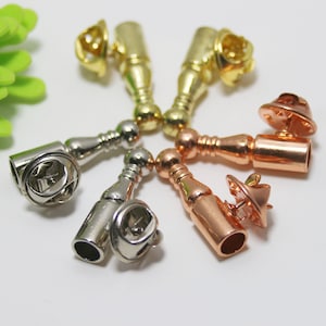 K&ouml;nnte beinhalten: Sechs Metall-Sicherheitsnadeln in verschiedenen Ausf&uuml;hrungen: Gold, Silber und Ros&eacute;gold. Jede Sicherheitsnadel hat einen runden Kopf und einen langen, zylindrischen K&ouml;rper.