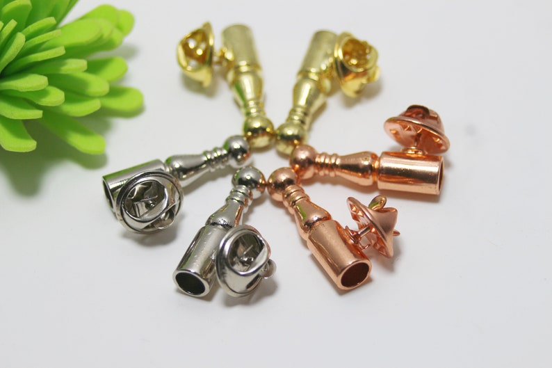 K&ouml;nnte beinhalten: Sechs Metall-Sicherheitsnadeln in verschiedenen Ausf&uuml;hrungen: Gold, Silber und Ros&eacute;gold. Jede Sicherheitsnadel hat einen runden Kopf und einen langen, zylindrischen K&ouml;rper.