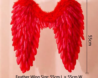 Puede incluir: Un par de alas de plumas de color rojo brillante con una textura suave y superpuesta. Las alas miden 55 cm de largo y 55 cm de ancho, según indican las líneas de medición. El texto inferior especifica una altura de ajuste de 140 cm a 160 cm.