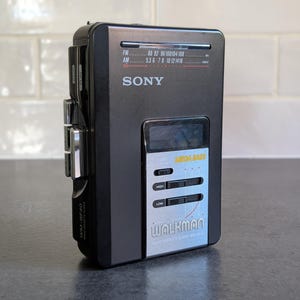 May include: A black Sony Walkman WM-BF40 radio cassette player with a silver control panel. The device features an AM/FM radio tuner display, Mega Bass settings, and physical playback buttons on the side. The front panel displays the Sony logo.