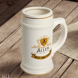 Könnte beinhalten: Ein weißer Keramik-Bierkrug mit goldener Verzierung und einem goldenen Wappen mit dem Buchstaben "A" und dem Namen "Allen" mit dem Text "Est. 1964" und "Best Dad Ever".