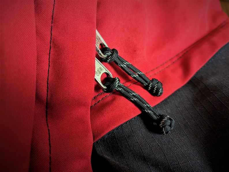 May include: Close-up of a red and black jacket with a zipper and black drawstrings. The zipper has a silver pull tab.