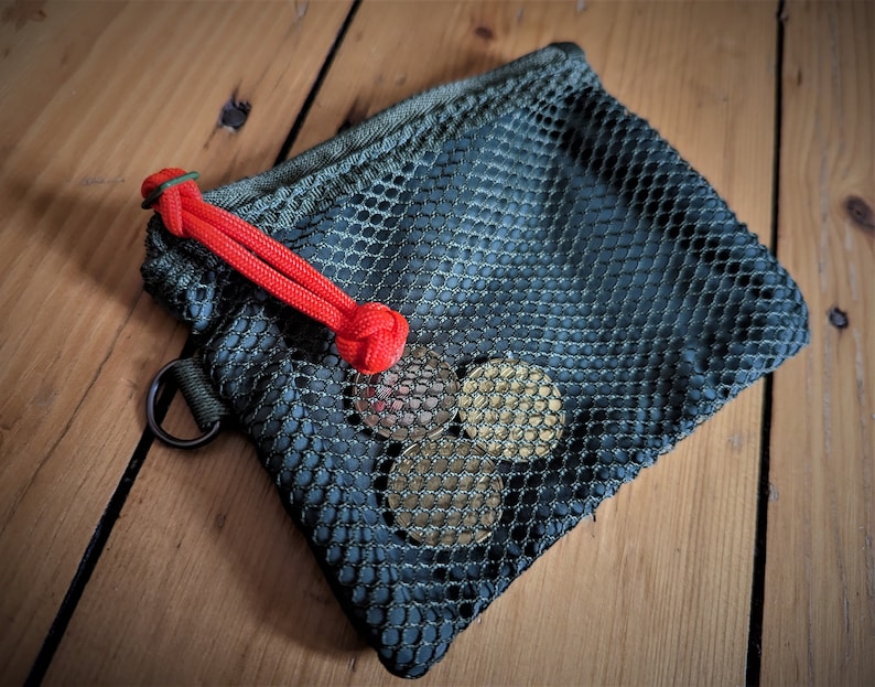 May include: A small green mesh drawstring bag with a red cord closure. The bag is filled with four gold-colored coins.