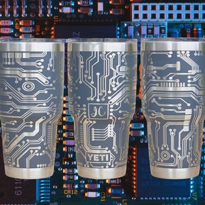 Puede incluir: Tres vasos de acero inoxidable con un diseño de placa de circuito plateado sobre un fondo gris. Los vasos están etiquetados con "YETI" y "JC".