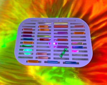 Può includere: Un vassoio viola con file di bacchette di vetro colorate. Le bacchette sono disposte a griglia e sono di vari colori, tra cui rosso, arancione, giallo, verde, blu e viola.