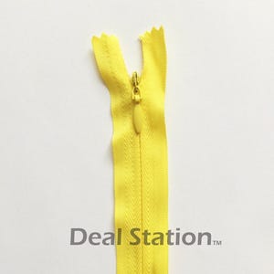 K&ouml;nnte beinhalten: Ein leuchtend gelber Rei&szlig;verschluss mit passendem Zipper vor wei&szlig;em Hintergrund. Der Rei&szlig;verschluss ist ge&ouml;ffnet und zeigt die Z&auml;hne und das Stoffband. Der Text "Deal Station" ist auf dem Rei&szlig;verschluss aufgedruckt.