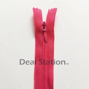 K&ouml;nnte beinhalten: Ein leuchtend pinkfarbener Rei&szlig;verschluss mit passendem Zipper vor wei&szlig;em Hintergrund. Die Z&auml;hne des Rei&szlig;verschlusses sind sichtbar, und das Stoffband hat ein dezentes Fischgr&auml;tmuster. Der Text "Deal Station" ist auf dem Band aufgedruckt.