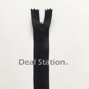 K&ouml;nnte beinhalten: Ein schwarzer Rei&szlig;verschluss mit geschlossenem Schieber vor wei&szlig;em Hintergrund. Das Rei&szlig;verschlussband hat ein Fischgr&auml;tenmuster. Der Text "Deal Station" ist auf dem Band aufgedruckt.