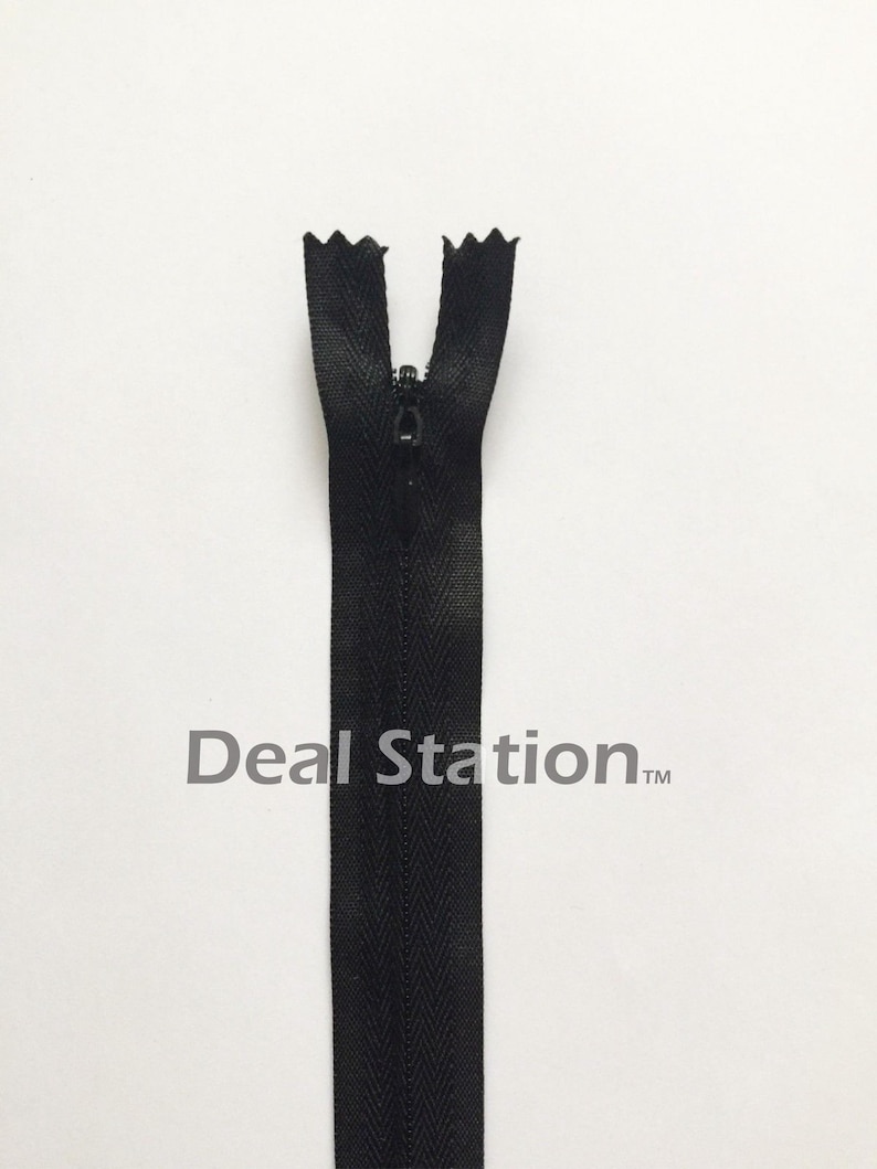 K&ouml;nnte beinhalten: Ein schwarzer Rei&szlig;verschluss mit geschlossenem Schieber vor wei&szlig;em Hintergrund. Das Rei&szlig;verschlussband hat ein Fischgr&auml;tenmuster. Der Text "Deal Station" ist auf dem Band aufgedruckt.