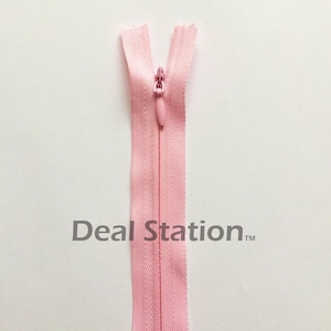 K&ouml;nnte beinhalten: Hellrosa Rei&szlig;verschluss mit passendem Zipper vor wei&szlig;em Hintergrund. Der Rei&szlig;verschluss ist oben ge&ouml;ffnet und zeigt die Z&auml;hne. Der Text "Deal Station" ist unten im Bild aufgedruckt.