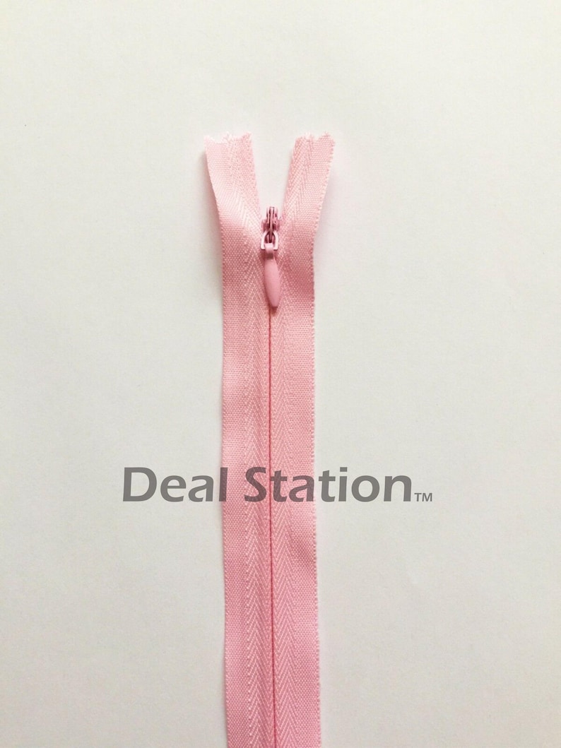 K&ouml;nnte beinhalten: Hellrosa Rei&szlig;verschluss mit passendem Zipper vor wei&szlig;em Hintergrund. Der Rei&szlig;verschluss ist oben ge&ouml;ffnet und zeigt die Z&auml;hne. Der Text "Deal Station" ist unten im Bild aufgedruckt.