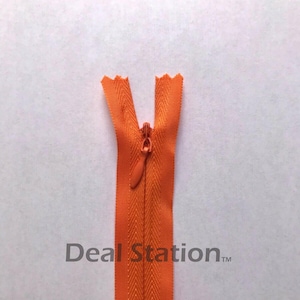 K&ouml;nnte beinhalten: Ein orangefarbener, unsichtbarer Rei&szlig;verschluss mit passendem Zipper vor wei&szlig;em Hintergrund. Die Z&auml;hne des Rei&szlig;verschlusses sind verdeckt, was einen nahtlosen Look erzeugt. Der Text "Deal Station" ist unten aufgedruckt.