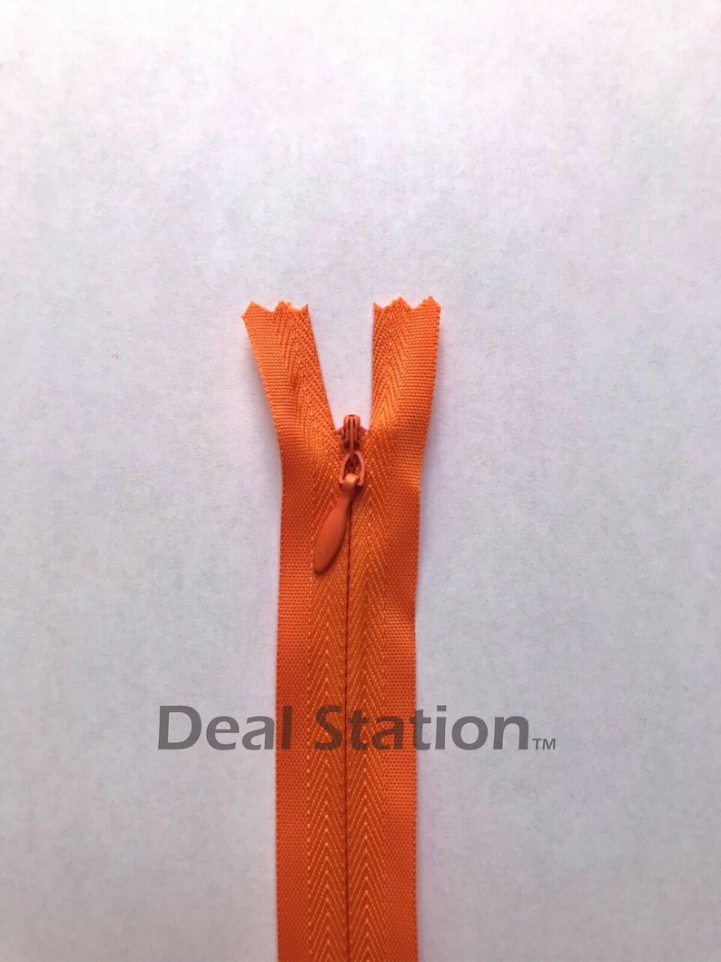 K&ouml;nnte beinhalten: Ein orangefarbener, unsichtbarer Rei&szlig;verschluss mit passendem Zipper vor wei&szlig;em Hintergrund. Die Z&auml;hne des Rei&szlig;verschlusses sind verdeckt, was einen nahtlosen Look erzeugt. Der Text "Deal Station" ist unten aufgedruckt.