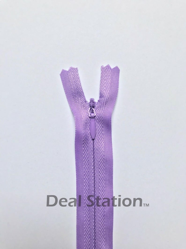 K&ouml;nnte beinhalten: Ein lavendelfarbener Rei&szlig;verschluss mit geschlossenem Schieber. Die Rei&szlig;verschlussz&auml;hne sind oben sichtbar, und der Stoff hat ein Fischgr&auml;tenmuster. Der Text "Deal Station" ist unten aufgedruckt.