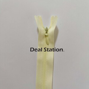 K&ouml;nnte beinhalten: Hellgelber Rei&szlig;verschluss mit Metall-Rei&szlig;verschlussanh&auml;nger. Der Rei&szlig;verschluss ist zentriert und vertikal vor einem wei&szlig;en Hintergrund ausgerichtet. Der Text "Deal Station" ist auf dem Rei&szlig;verschluss aufgedruckt.