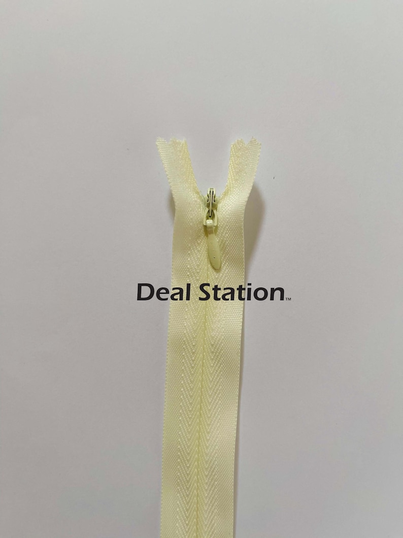 K&ouml;nnte beinhalten: Hellgelber Rei&szlig;verschluss mit Metall-Rei&szlig;verschlussanh&auml;nger. Der Rei&szlig;verschluss ist zentriert und vertikal vor einem wei&szlig;en Hintergrund ausgerichtet. Der Text "Deal Station" ist auf dem Rei&szlig;verschluss aufgedruckt.