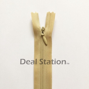 K&ouml;nnte beinhalten: Beigefarbener, unsichtbarer Rei&szlig;verschluss mit goldfarbenem Rei&szlig;verschlussanh&auml;nger. Der Rei&szlig;verschluss ist auf wei&szlig;em Hintergrund zentriert. Der Text "Deal Station" ist grau darunter gedruckt.