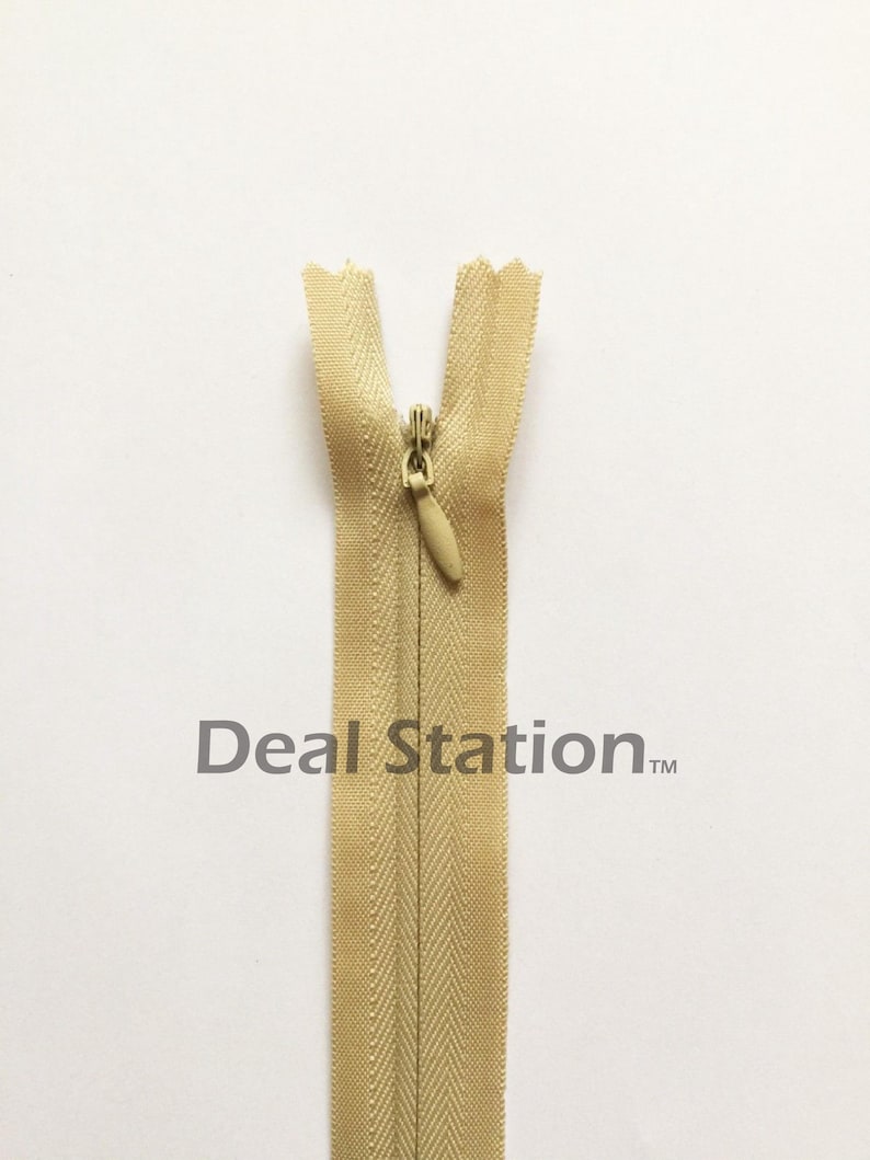 K&ouml;nnte beinhalten: Beigefarbener, unsichtbarer Rei&szlig;verschluss mit goldfarbenem Rei&szlig;verschlussanh&auml;nger. Der Rei&szlig;verschluss ist auf wei&szlig;em Hintergrund zentriert. Der Text "Deal Station" ist grau darunter gedruckt.