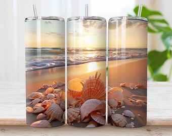 May include: A cylindrical stainless steel tumbler featuring a wrap-around print of a sandy beach at sunset with scattered seashells in the foreground. The design includes a clear plastic lid and a matching straw, showcasing a warm golden color palette.