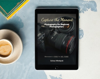 May include: A black tablet computer displaying an ebook cover with the title "Capture the Moment: Photography for Beginner Photographers". The cover features a close-up of a camera lens and the text "Become a PRO in NO TIME" and "Zachary Mikołajczak".
