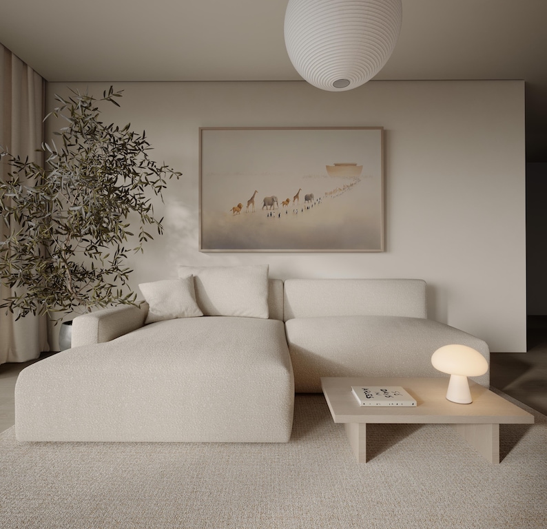 May include: A modern living room with a cream-colored sectional sofa, a light wood coffee table, and a small mushroom-shaped lamp. A framed artwork depicts animals walking towards a boat. A large, round pendant light hangs from the ceiling.