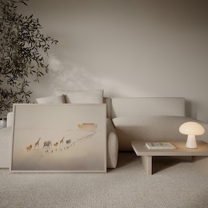 May include: A framed art print depicting a line of animals, including giraffes and elephants, walking towards a boat. The artwork is in soft, neutral tones and is displayed on a beige sofa. A small, white mushroom-shaped lamp sits on a wooden side table.