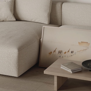 May include: A framed art print depicting a procession of animals, including lions, giraffes, and elephants, walking towards an ark. The artwork is set against a muted, beige background. A light wood coffee table holds books and a decorative bowl.