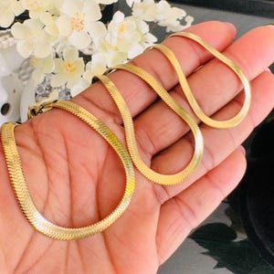 Puede incluir: Un conjunto de cuatro collares de cadena de serpiente dorada de diferentes longitudes. Las cadenas están hechas de un metal liso y brillante y tienen un diseño clásico y elegante.