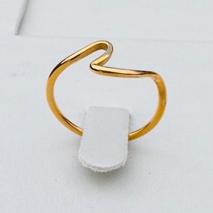 May include: A gold-coloured ring with a wavy design. The ring is on a white display stand.