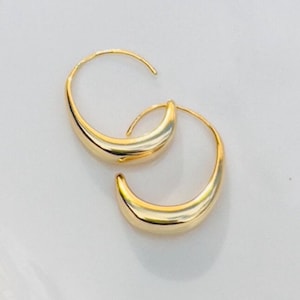 May include: A pair of gold hoop earrings with a curved, smooth design. The earrings are simple and elegant.