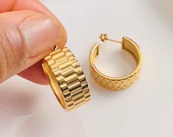 May include: A pair of gold hoop earrings with a textured, geometric design. The earrings are thick and have a wide diameter.