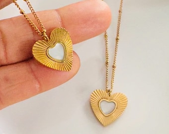 May include: Two gold necklaces with heart pendants. Each pendant features a sunburst design with a white mother-of-pearl center.