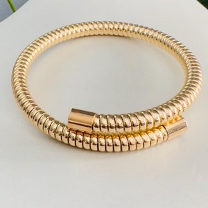 May include: A gold-toned, coiled, flexible bracelet with a smooth, polished finish.