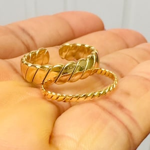 May include: Two gold-toned rings with a twisted rope design. The rings are stacked on top of each other.