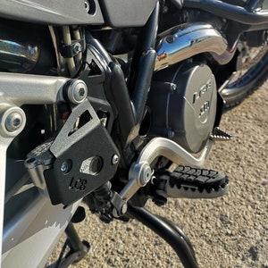 May include: Close-up of a black motorcycle engine guard with the text "LC8" on it. The guard is attached to a silver motorcycle frame.