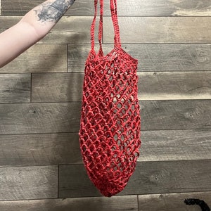 May include: A red crocheted mesh bag with a long handle. The bag is made of a thick, textured yarn and has a loose, open weave.