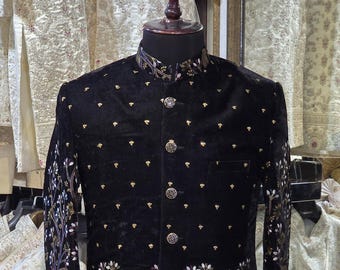 Könnte beinhalten: Schwarze Samtjacke mit aufwendiger Stickerei mit Bäumen und Hirschen. Die Jacke hat einen Stehkragen und dekorative Knöpfe. Die Ärmel und der Saum sind mit detaillierten Mustern verziert. Ein formelles Kleidungsstück für besondere Anlässe.