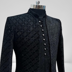 Pode incluir: Casaco formal preto com gola alta e padrão de losangos. O casaco tem fecho de botões com botões decorativos. A camada interna tem um design bordado. O casaco é exibido em um manequim.