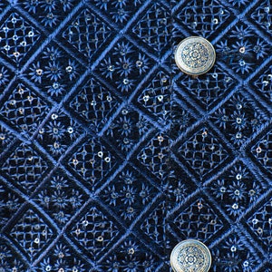 K&ouml;nnte beinhalten: Nahaufnahme eines marineblauen Stoffes mit einem aufwendigen Stickmuster. Das Design zeigt Rauten, Blumenmotive und kleine Pailletten. Zwei dekorative, runde Kn&ouml;pfe mit floralem Design sind sichtbar.