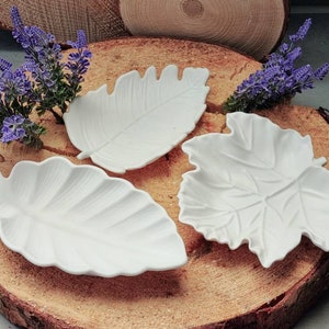 Könnte beinhalten: Drei weiße, keramikförmige, blattförmige Schalen auf einer Holzoberfläche. Die Schalen sind in einem dreieckigen Muster angeordnet.