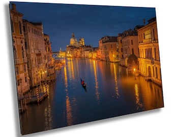 May include: A night view of a canal in Venice, Italy. The canal is lined with buildings and there is a gondola in the water. The buildings are lit up and the water is reflecting the lights.