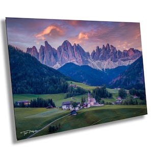 May include: A picturesque landscape with a small village nestled in a valley surrounded by majestic mountains. The sky is a vibrant pink and orange, creating a stunning sunset over the mountain peaks.