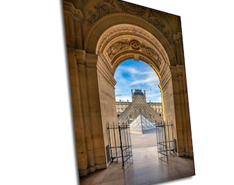 May include: A view of the Louvre Pyramid in Paris, France, seen through an arched doorway. The doorway is made of stone and has a decorative archway. The pyramid is made of glass and is surrounded by a courtyard.