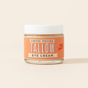 May include: A small glass jar of coffee-infused tallow eye cream with a white lid. The label is orange with white text that reads "Coffee Infused Tallow Eye Cream". A red "LM" logo is on the right side.