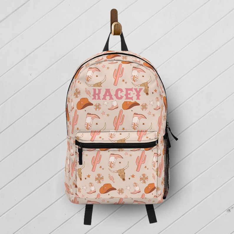 Personalized pink western cowgirl backpack for girls with custom name printed on the front, back-to-school book bag with cactus and cowboy boot print.
