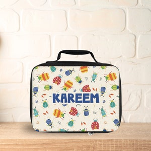 May include: A white lunch bag with a black handle and zipper. The bag has a colorful pattern of bugs and the name "KAREEM" printed in blue.